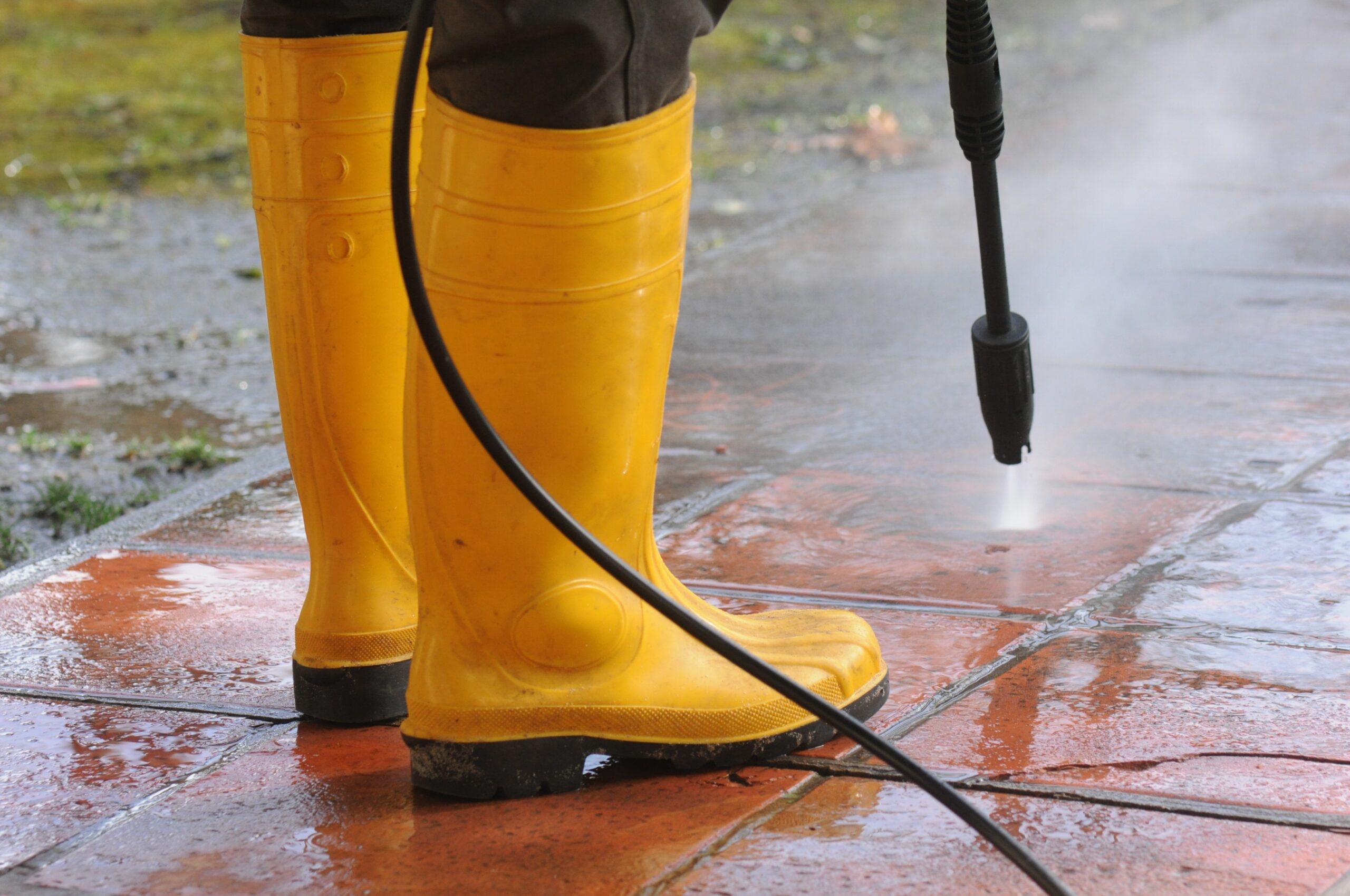 Person wearing yellow rubber boots with high-pressure water nozzle cleaning the dirt in the tiles north fort myers grass image